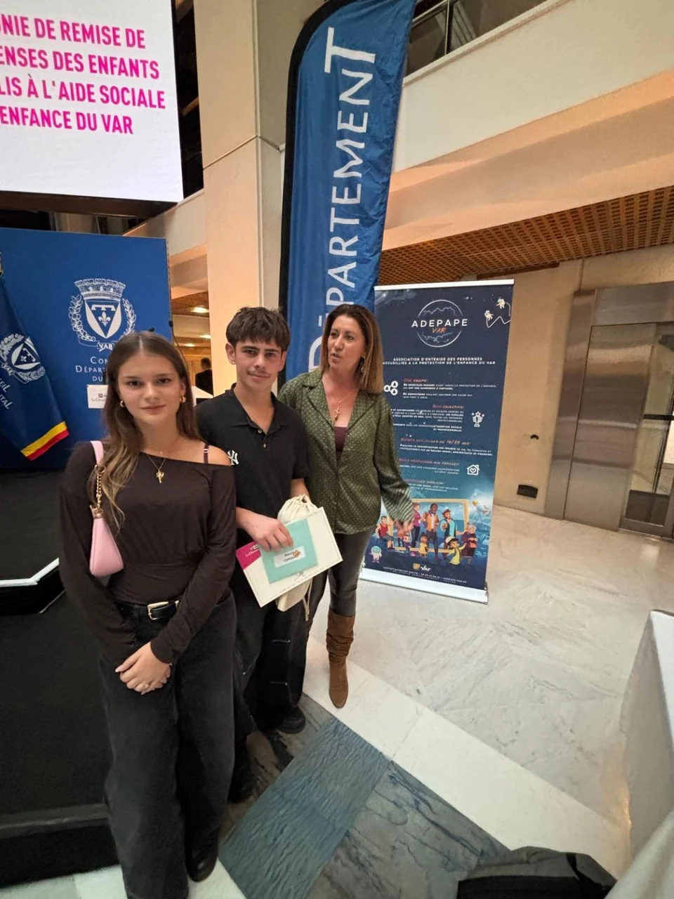 Trois personnes à la Fête de la Réussite, devant une affiche de l’ADEPAPE Var.