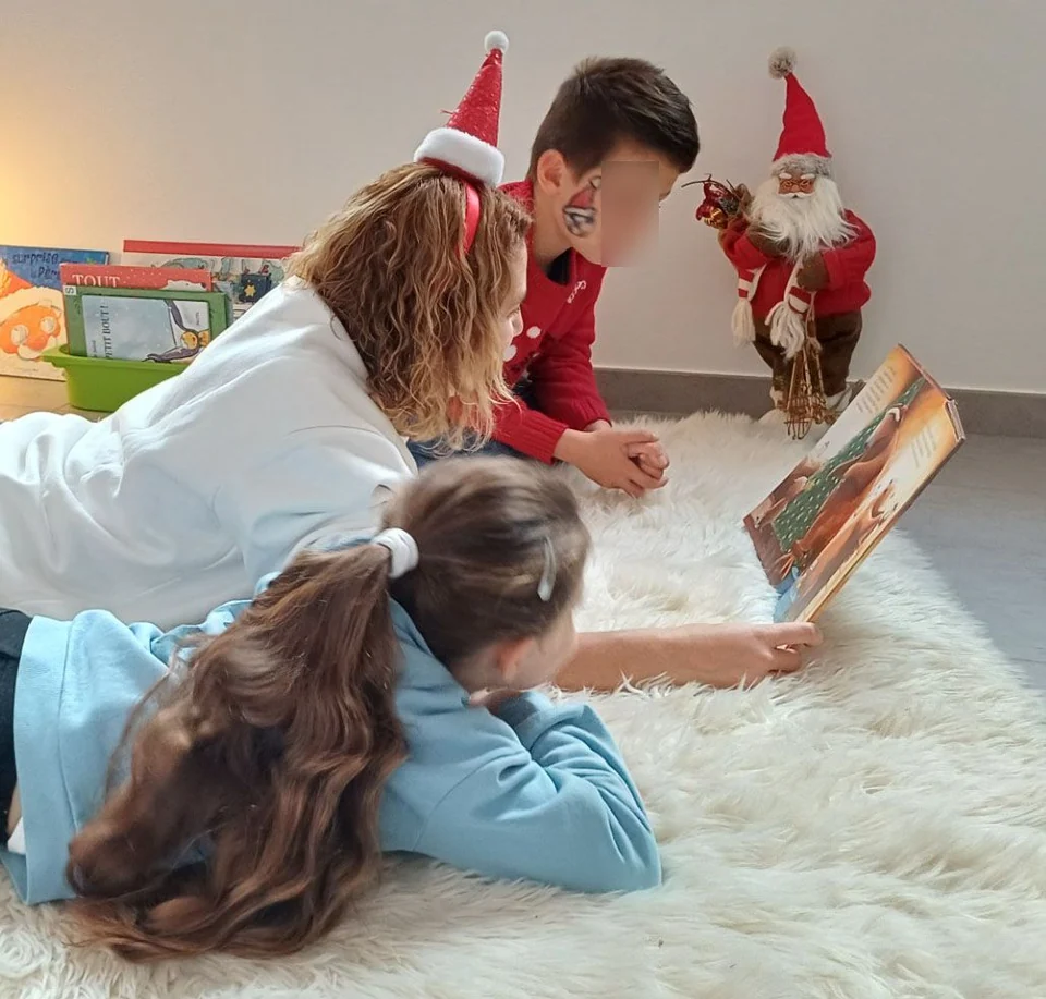 Une adulte et des enfants découvrent un livre parmi les cadeaux de Noël.