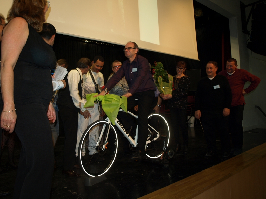 Un participant tient le vélo offert sur scène, entouré des autres invités.