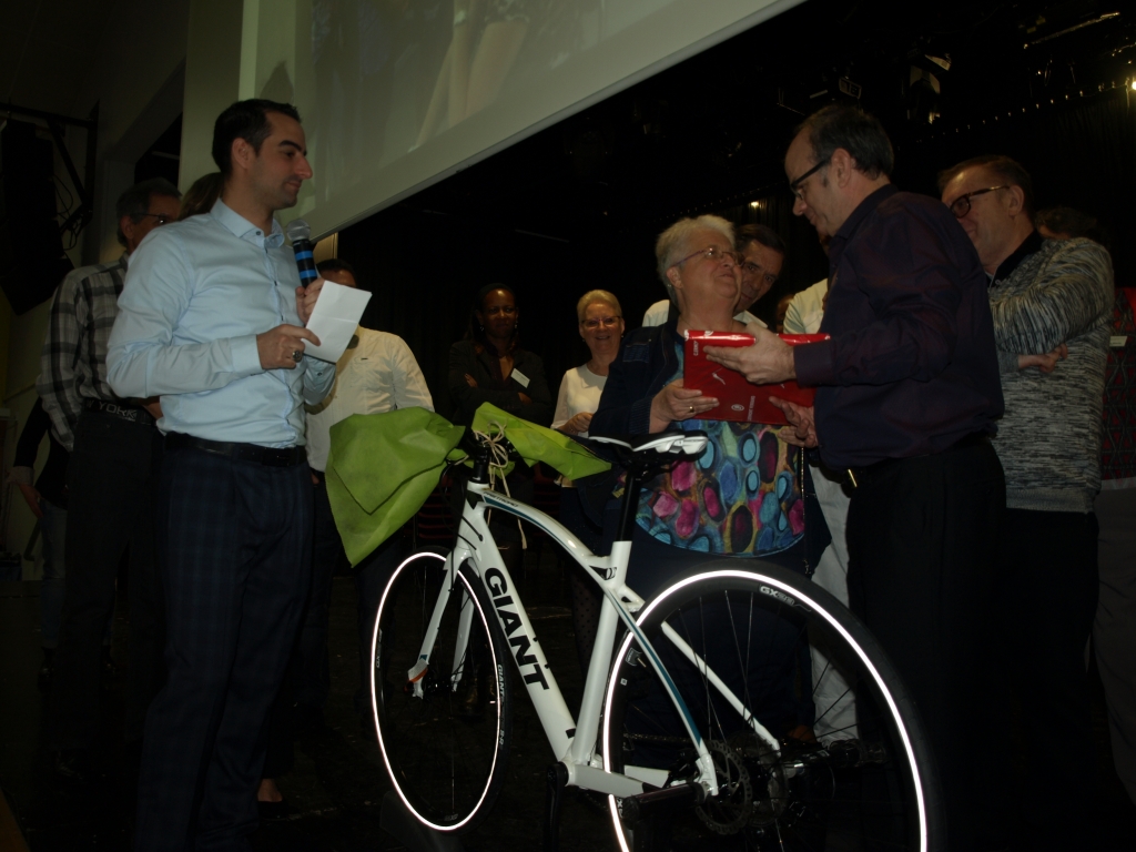 Remise d’un cadeau sur scène, à côté du vélo décoré d’un grand ruban vert.
