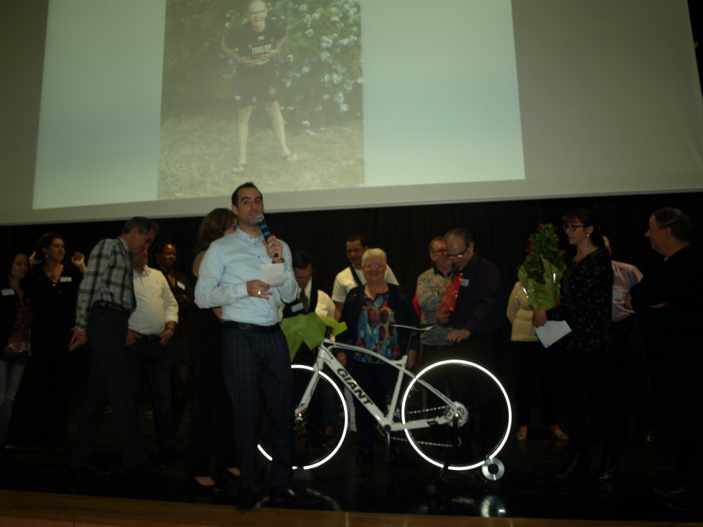 Un intervenant prend la parole au milieu du groupe, près du vélo offert.