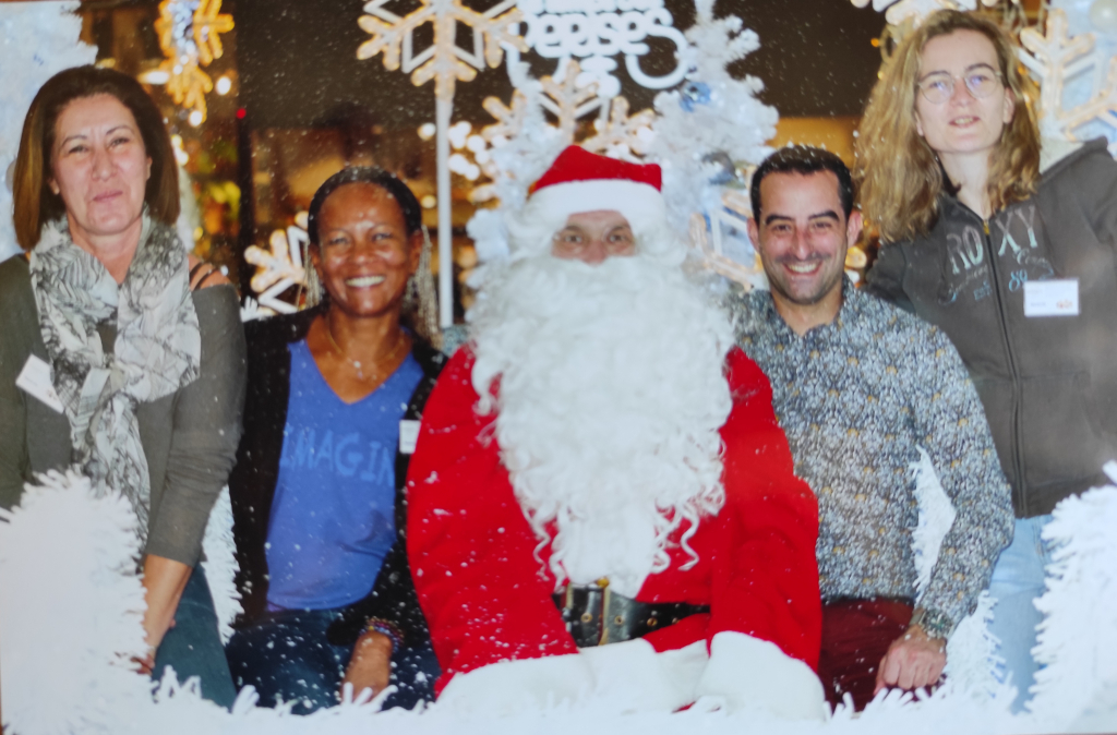 Quatre participants posent autour du Père Noël parmi les décorations blanches.