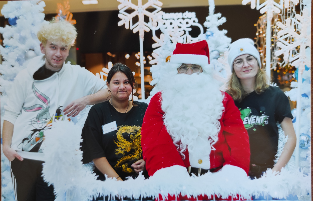 Quatre participants réunis avec le Père Noël derrière une rambarde décorée de neige artificielle.