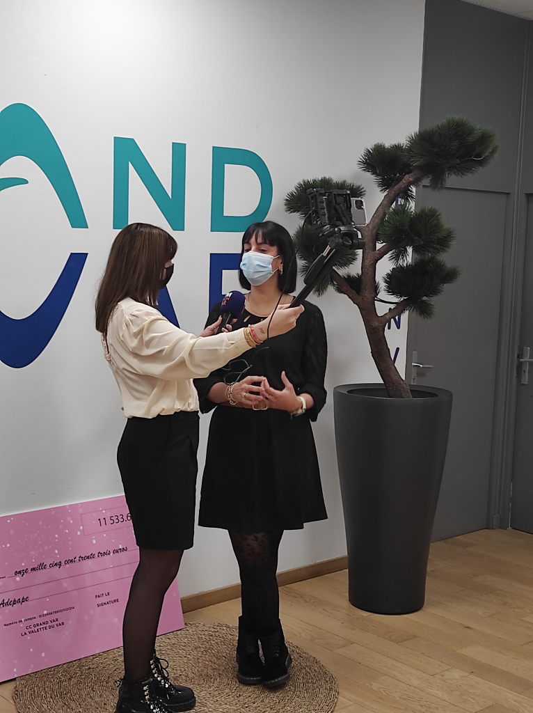 Une personne répond à une interview au micro devant le logo Grand Var.