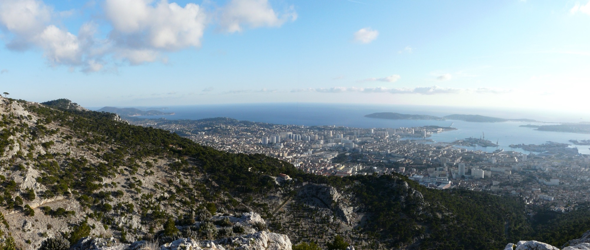 Vue panoramique de la ville de Toulon et de sa rade, depuis les hauteurs, sous un ciel dégagé.