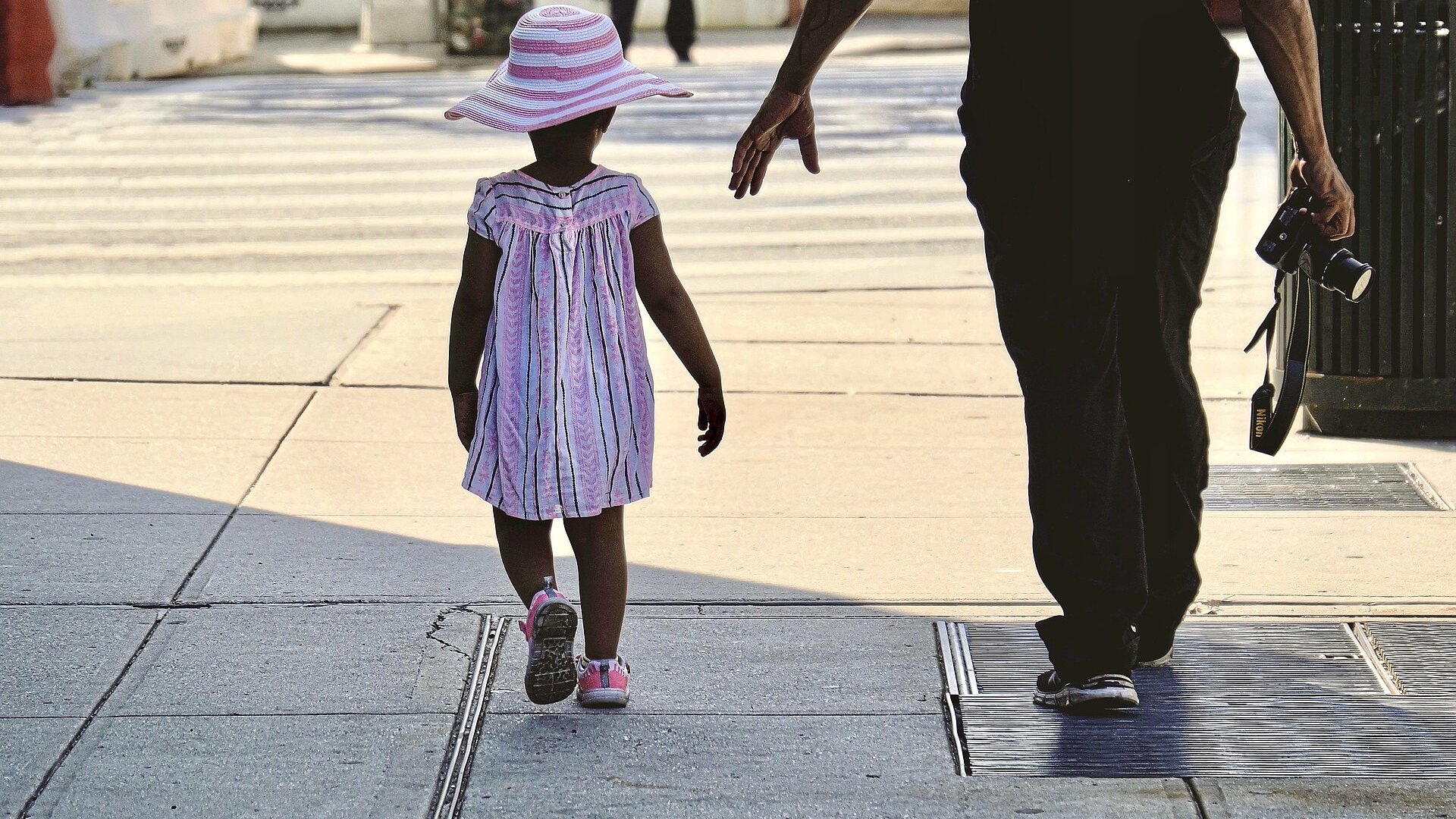 Un adulte et une enfant marchent côte à côte sur un trottoir.