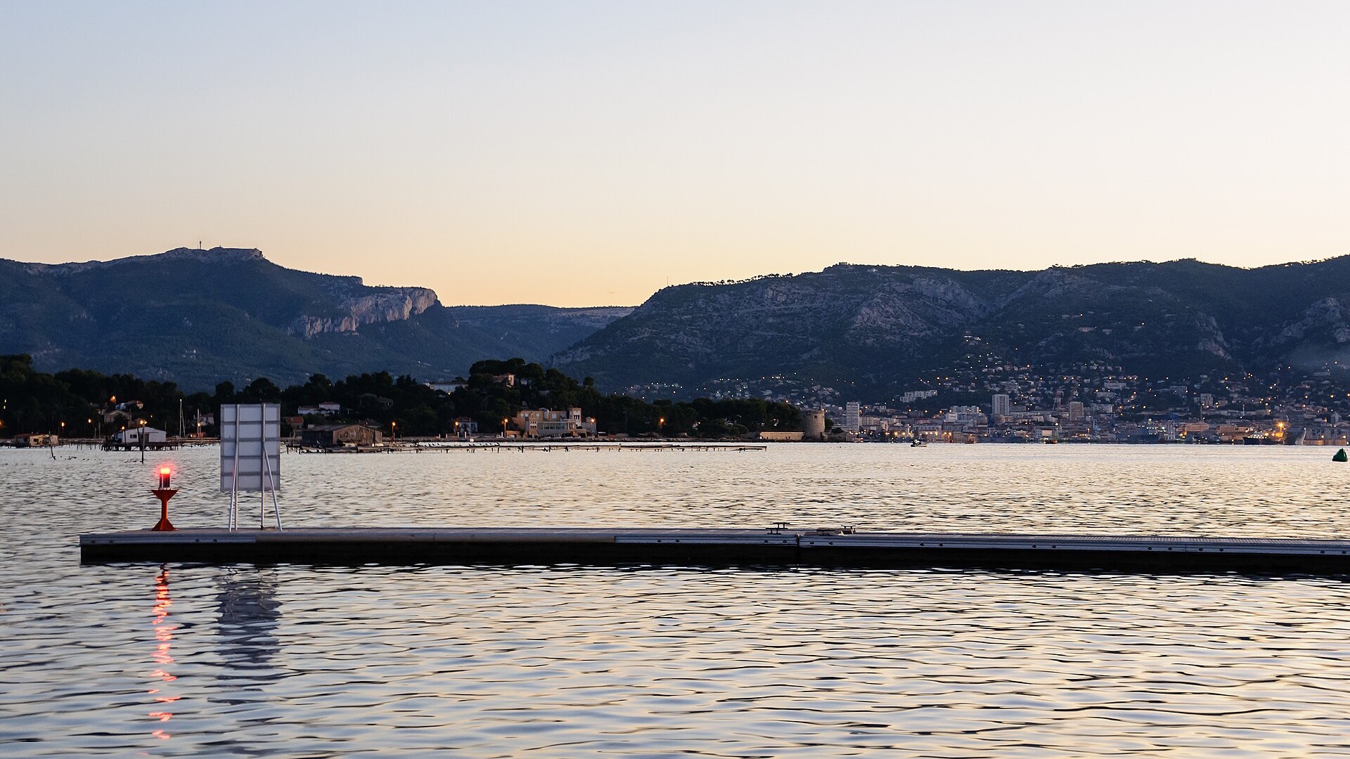 La petite rade de Toulon au crépuscule, vue depuis Saint-Mandrier-sur-Mer, avec la ville de Toulon éclairée au fond.