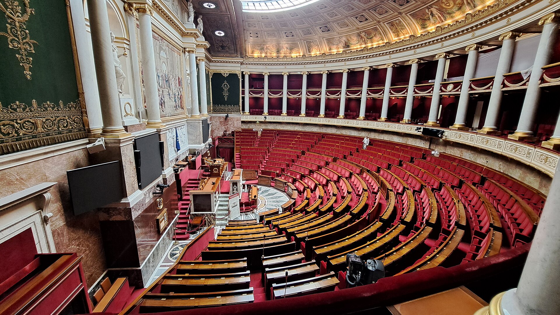 Vue de l'hémicycle vide de l'Assemblée nationale, à Paris, avec ses bancs rouges disposés en demi-cercle.