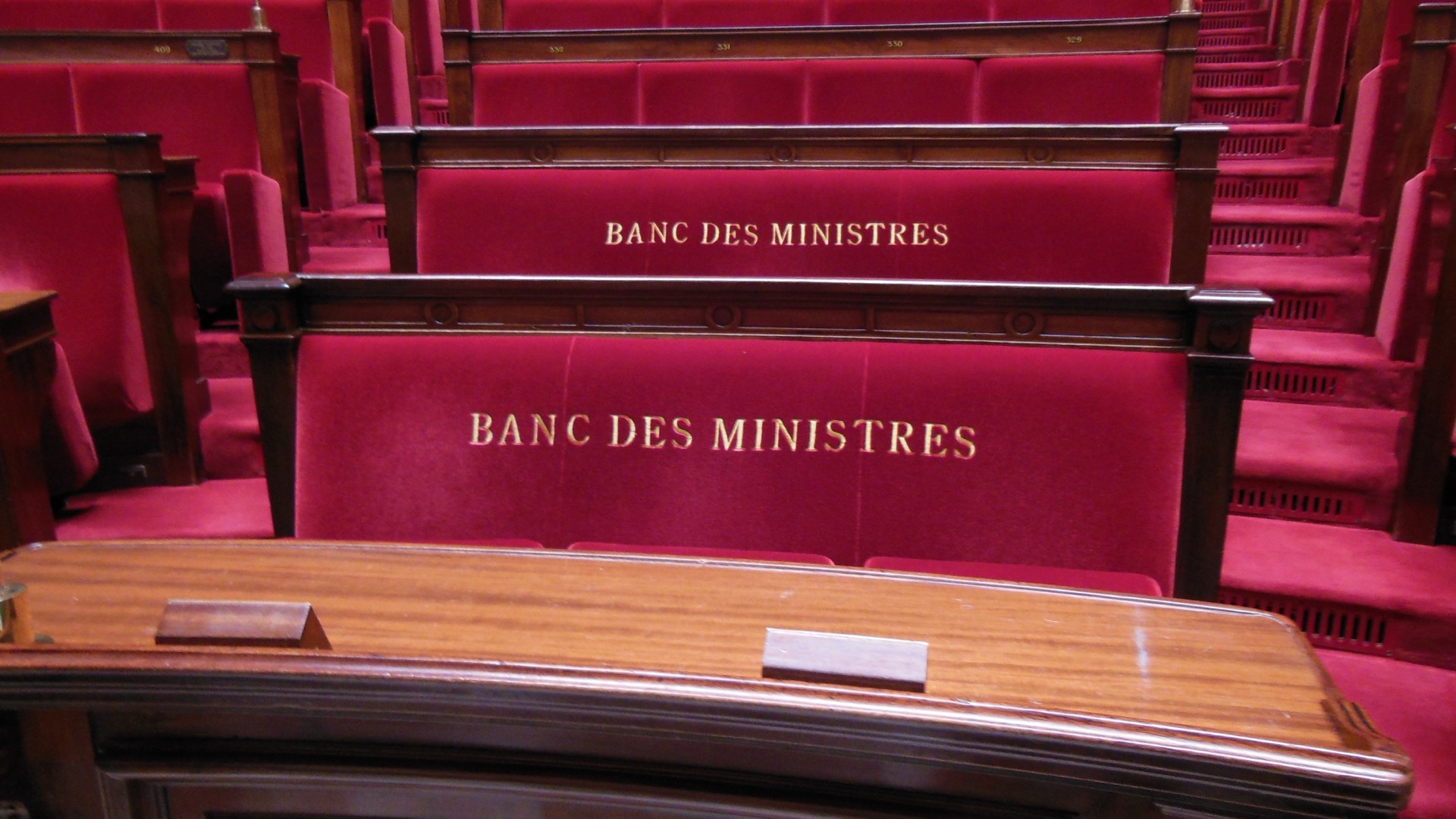 Les sièges rouges portant l’inscription « Banc des ministres ».