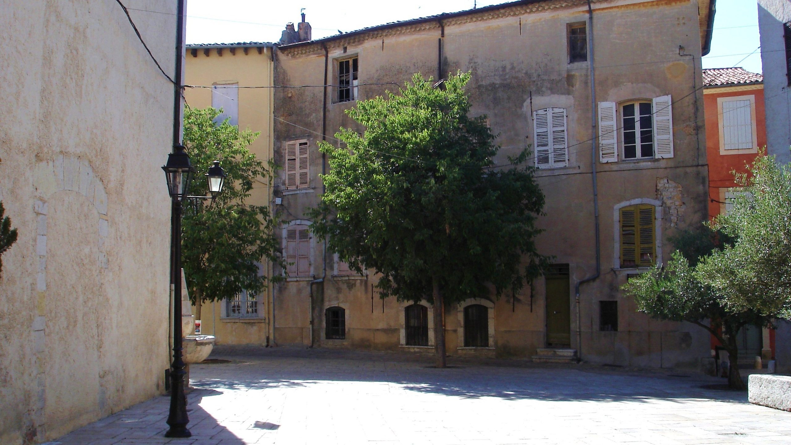 Une place ombragée de la vieille ville de Brignoles, dans le Var, bordée de façades provençales aux volets colorés.