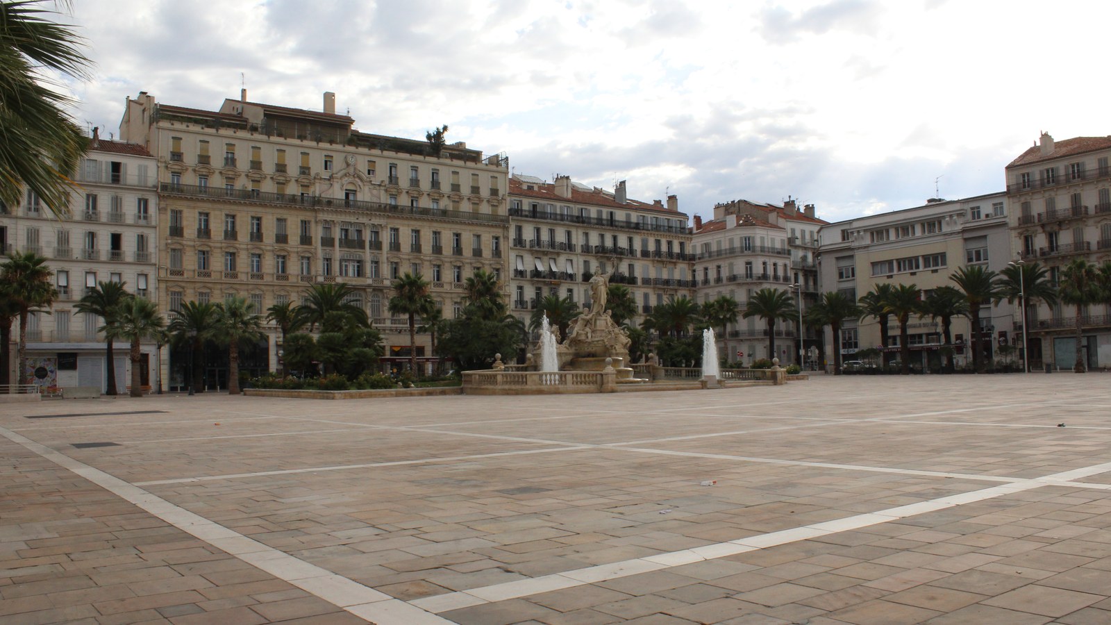 La place de la Liberté, vaste esplanade pavée au cœur de Toulon, bordée d'immeubles anciens et de palmiers, avec la fontaine de la Fédération