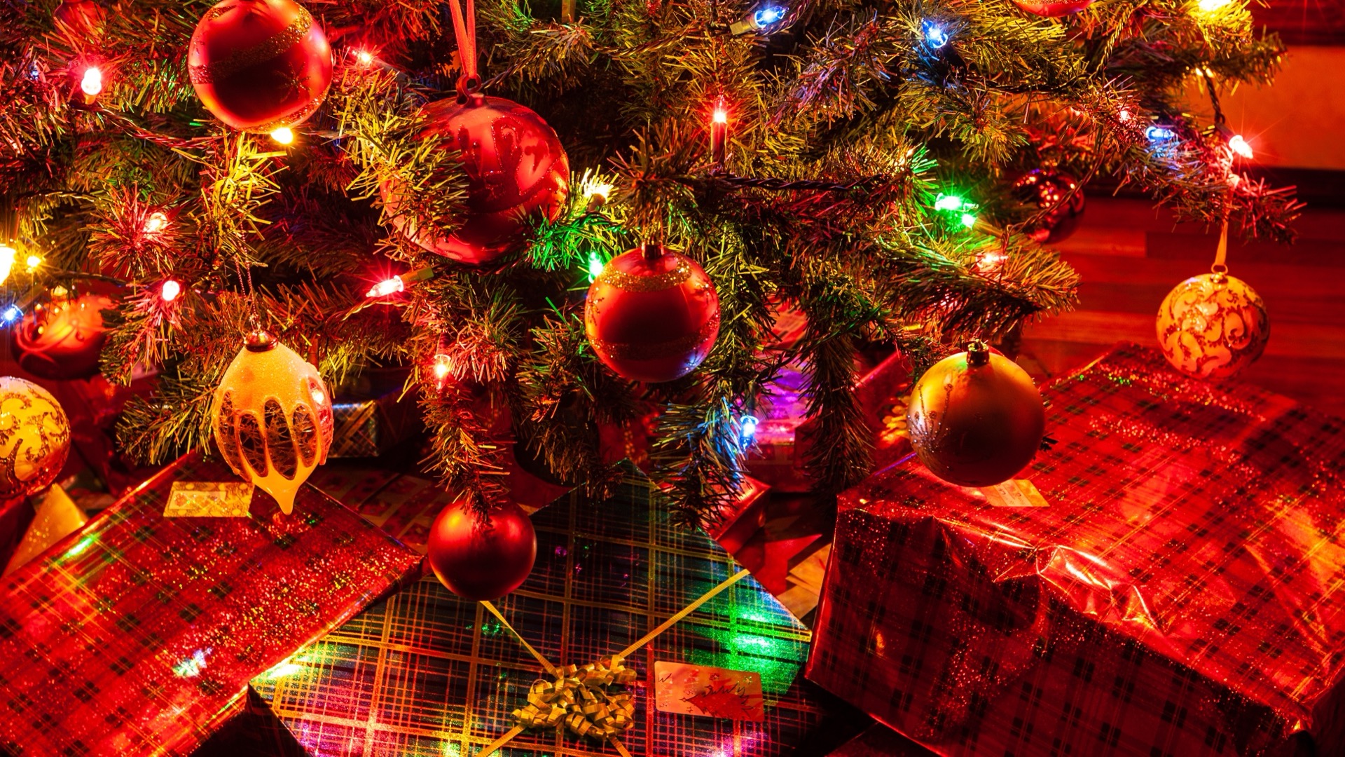 Sapin de Noël décoré de boules rouges et de guirlandes lumineuses, avec des cadeaux emballés disposés à son pied