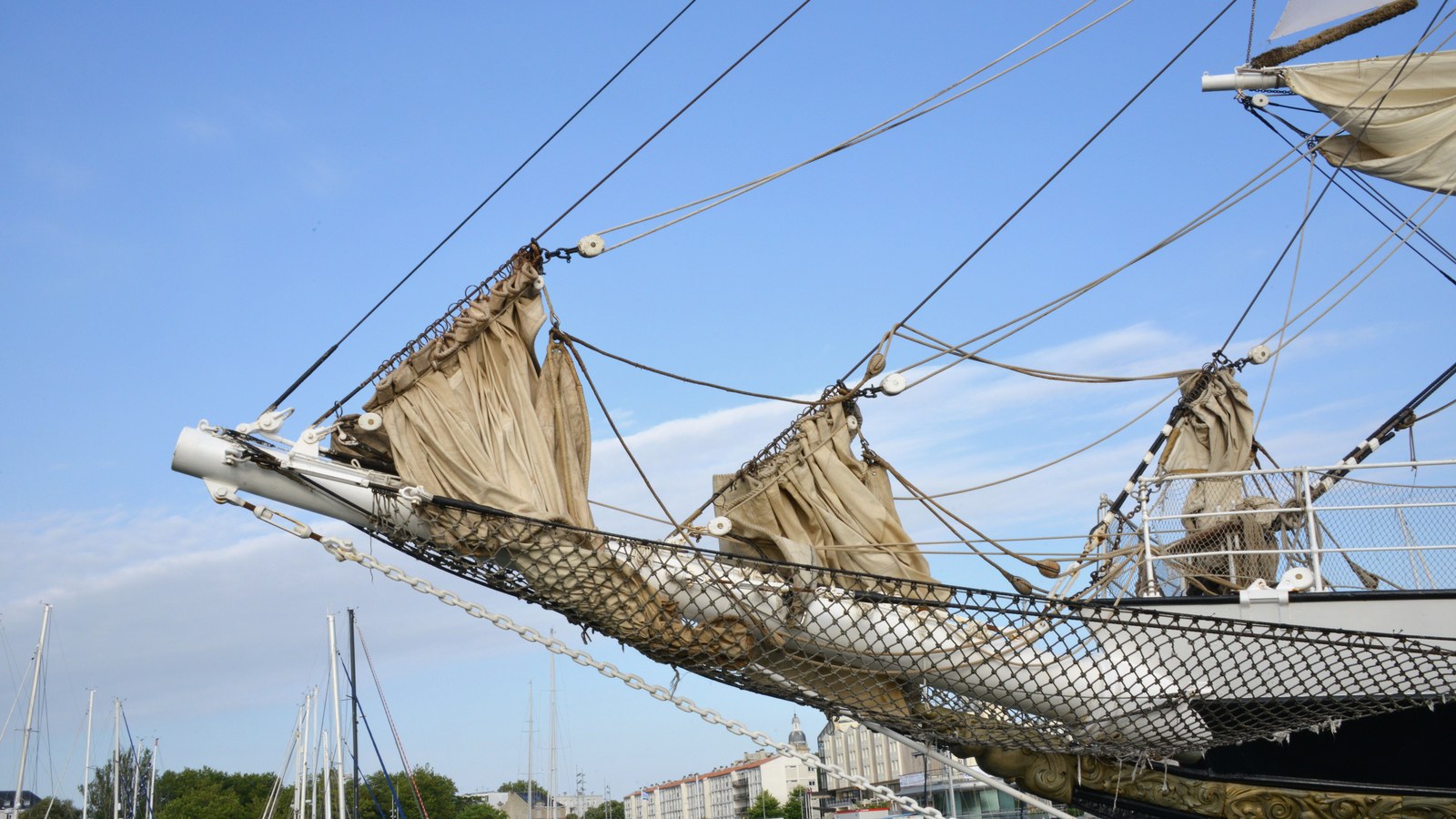 Le trois-mâts barque Belem, mâts et voiles ferlées sous un ciel bleu, amarré dans un port.