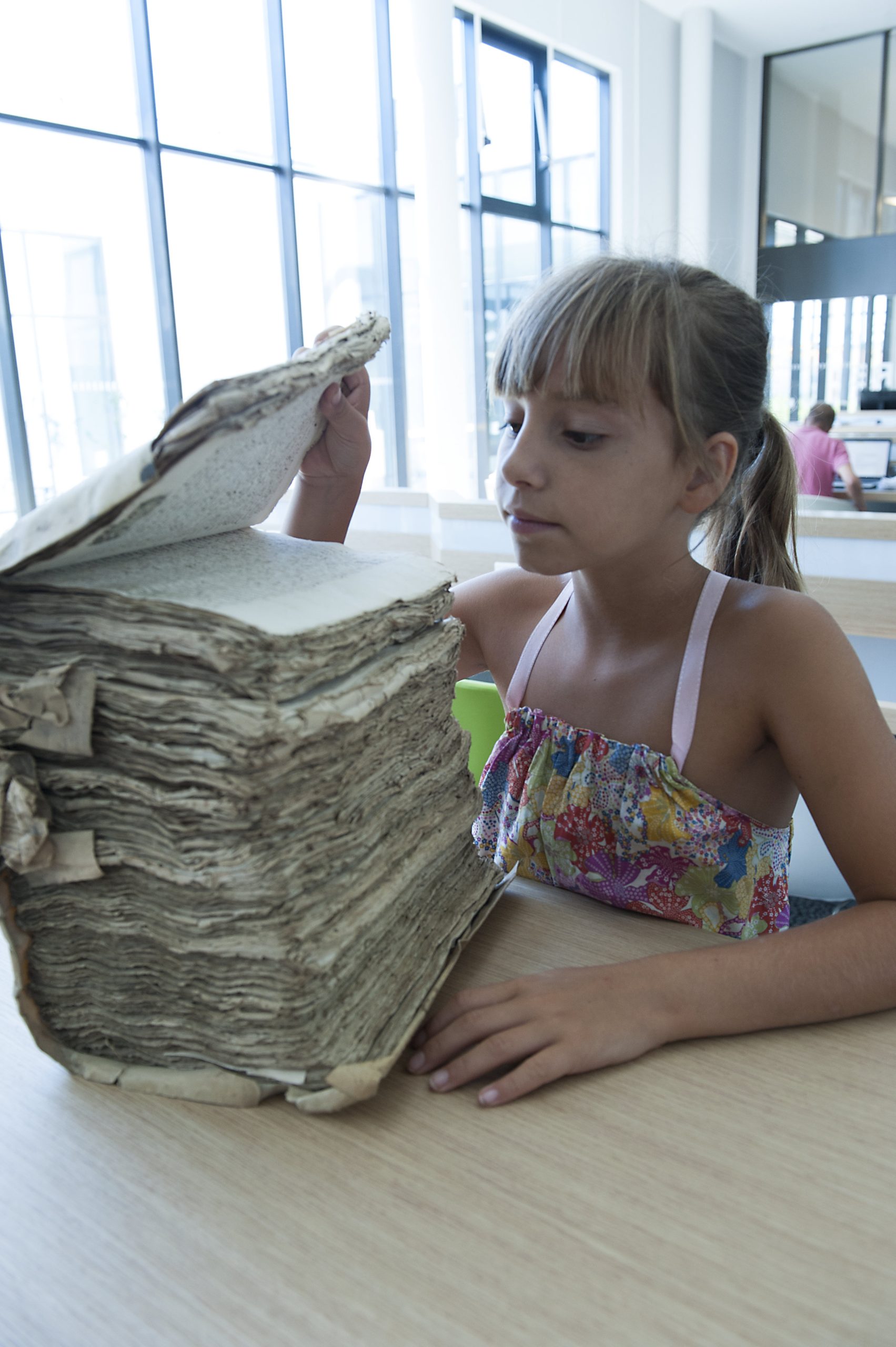 Une jeune visiteuse consulte un registre ancien dans un espace d’archives.