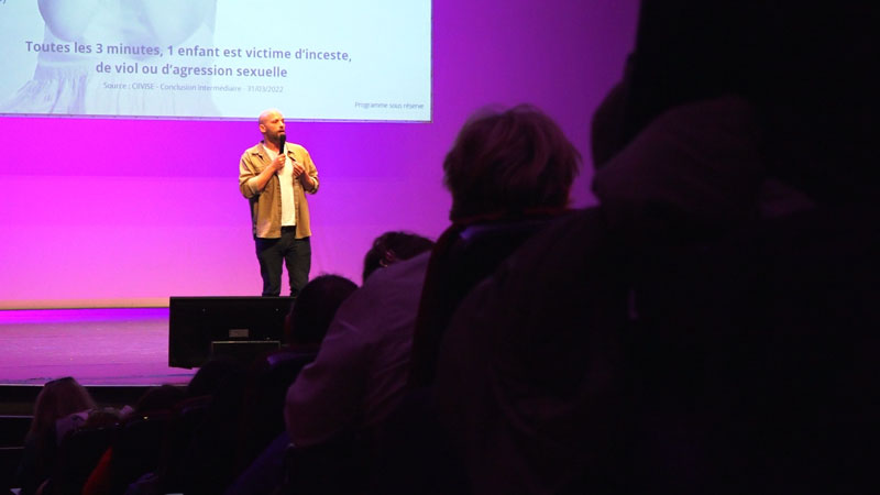 Les intervenants d’une conférence sur une scène éclairée en violet.